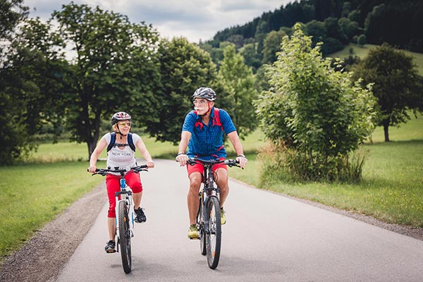 Zwei Radfahrer unterwegs auf einer Straße - im Hintergrund wundere blühende Bäume