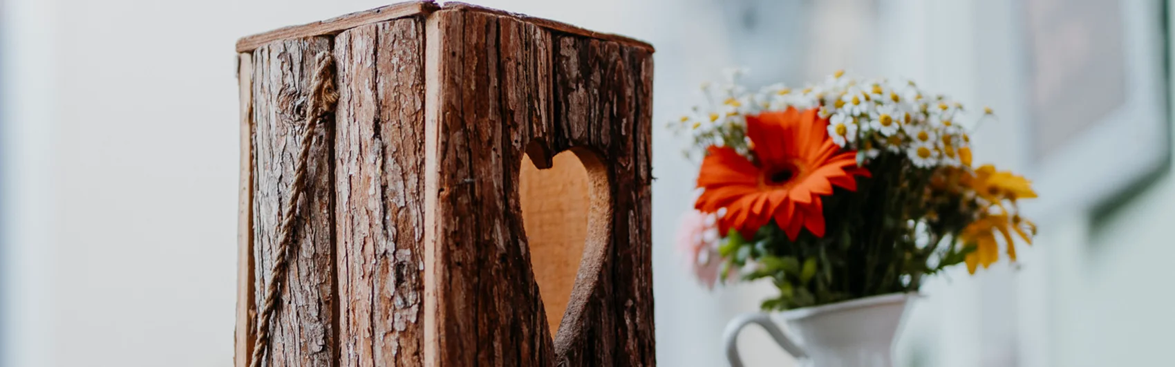 Im linken Bildbereich wurde aus Rinde ein großes Teelicht mit Herz gebaut und auf der rechten Seite befindet sich eine Wase mit einem kleinen Blumensträußchen.